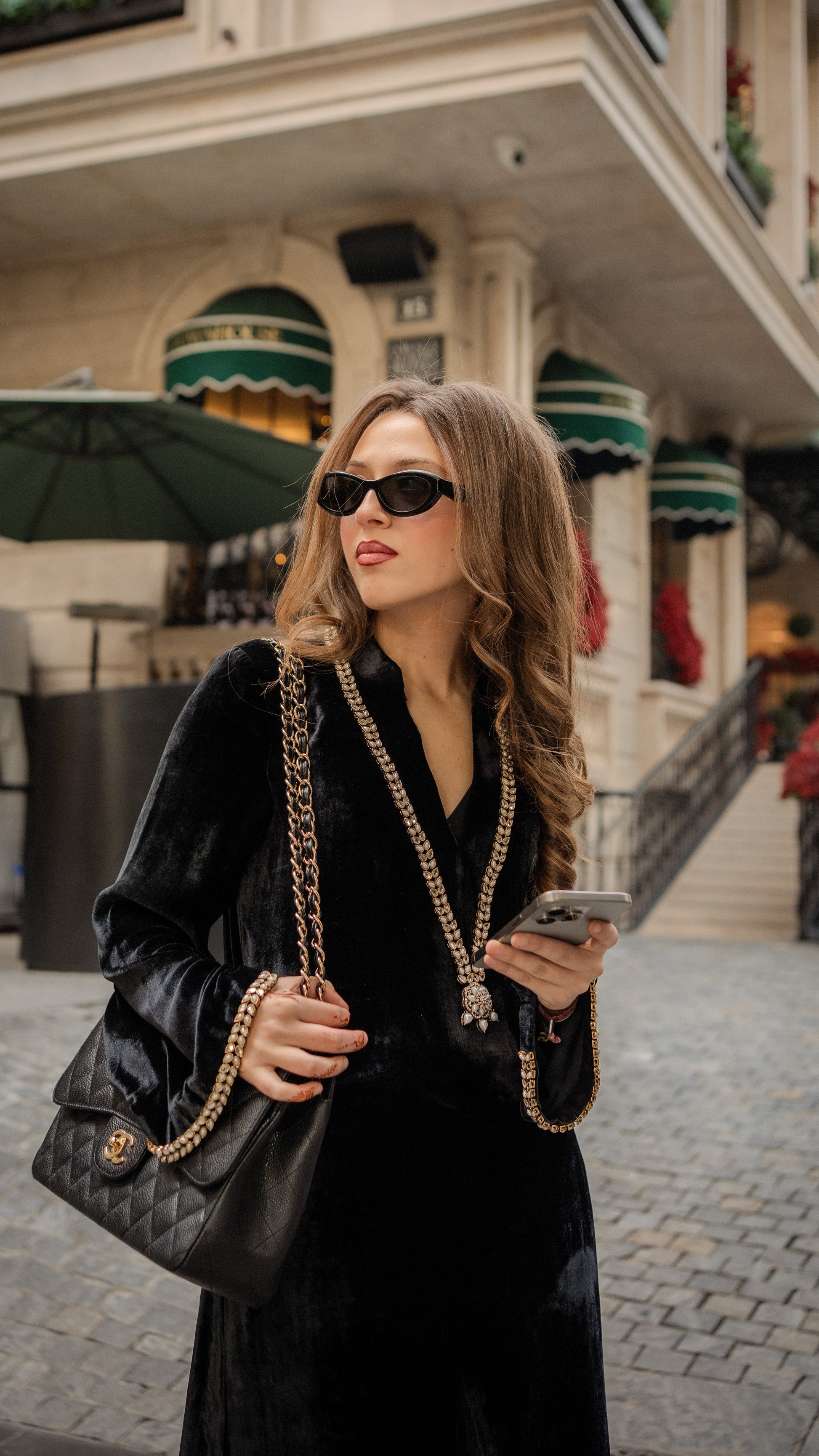 Woman in black outfit with sunglasses and a handbag walking on a street.