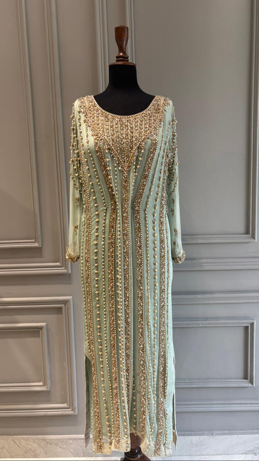 Mannequin wearing a light green dress with gold embellishments against a gray paneled wall.